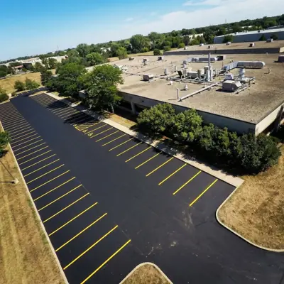 Aerial view of a newly paved asphalt parking lot with crisp yellow line striping beside a commercial building in the GTA