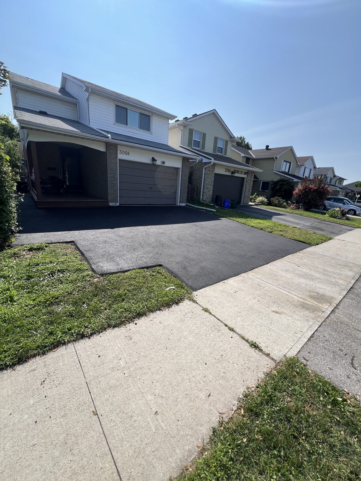 Newly paved smooth asphalt driveway leading to a two-car garage at a GTA home with green lawn and concrete walkway