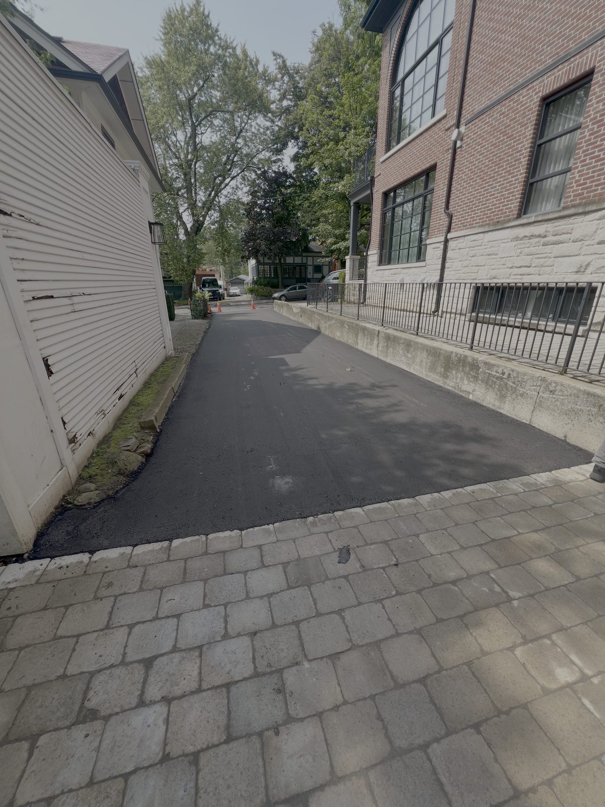 Freshly paved asphalt laneway running between two buildings and finishing against interlock stone pavers in the Greater Toronto Area