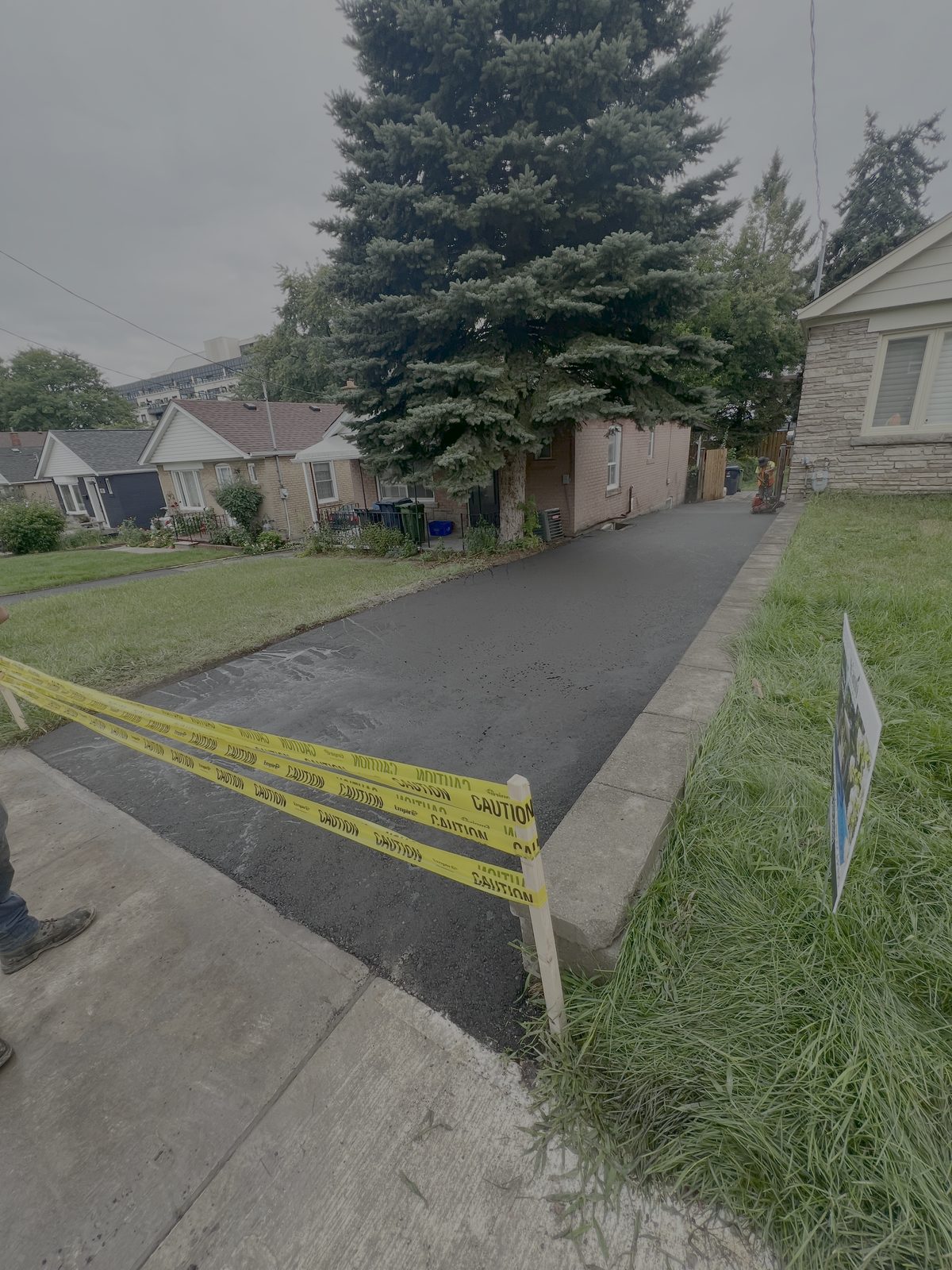 Newly paved residential asphalt driveway with caution tape and concrete curbing in a Toronto GTA neighbourhood