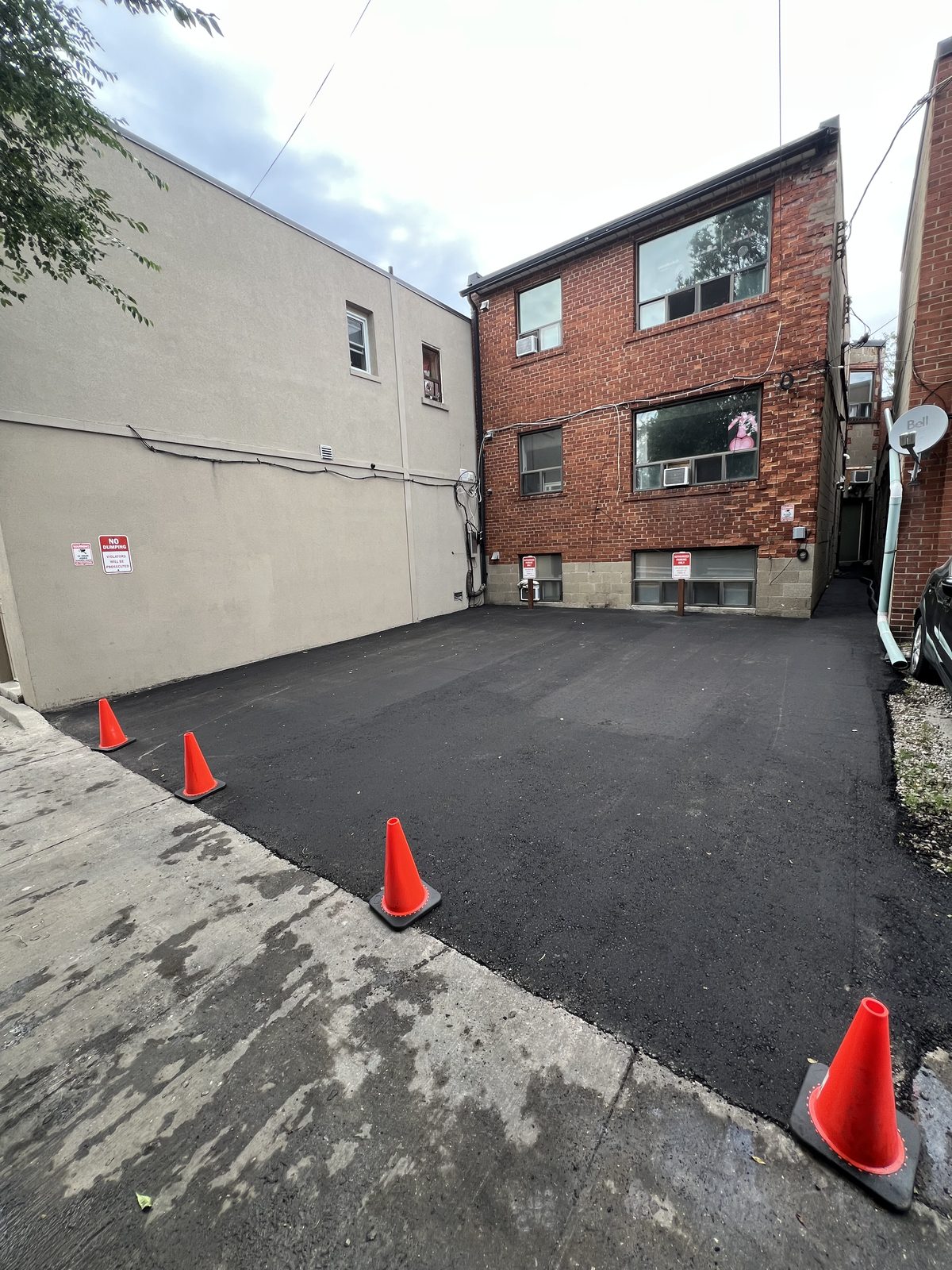Newly paved asphalt parking lot behind a brick apartment building with safety cones in the GTA