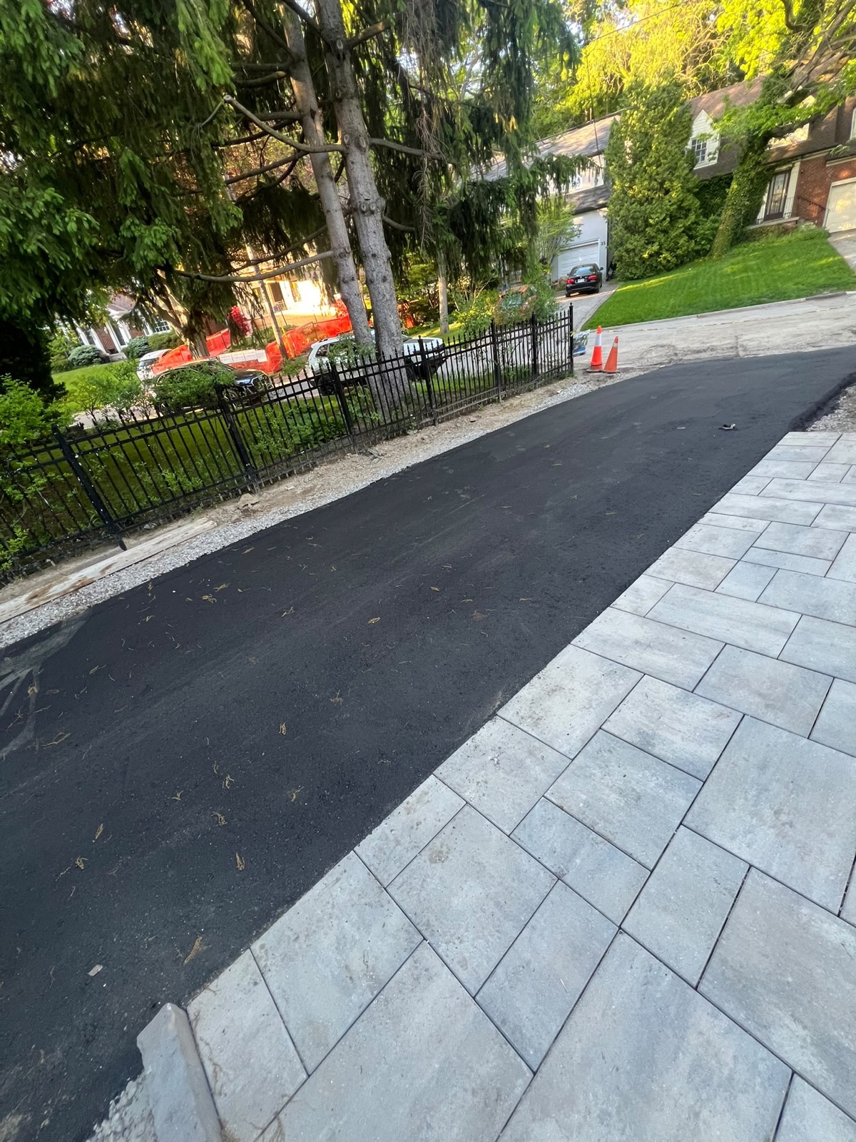 New asphalt driveway with a grey paver apron and wrought-iron fence