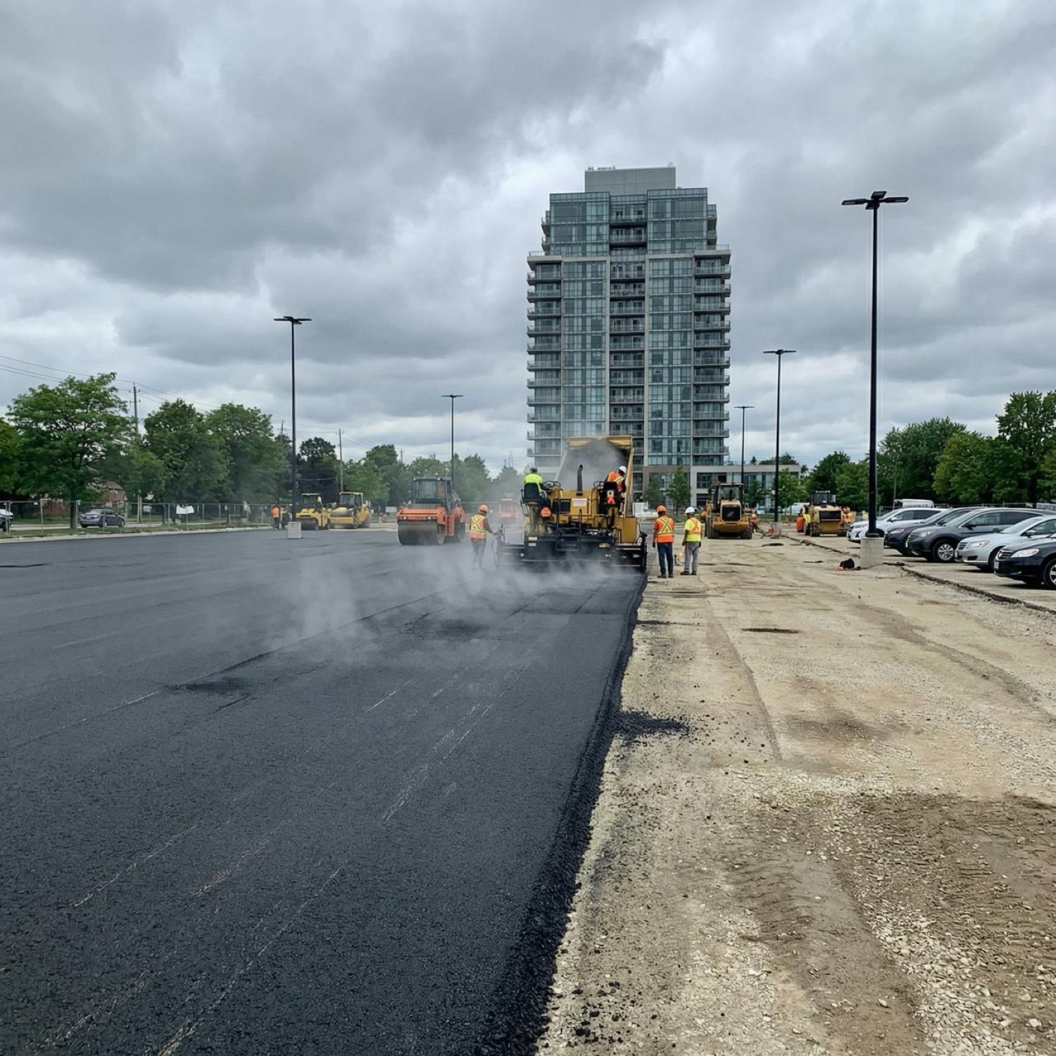 Magnum crew paving a large commercial parking lot with a condo tower behind
